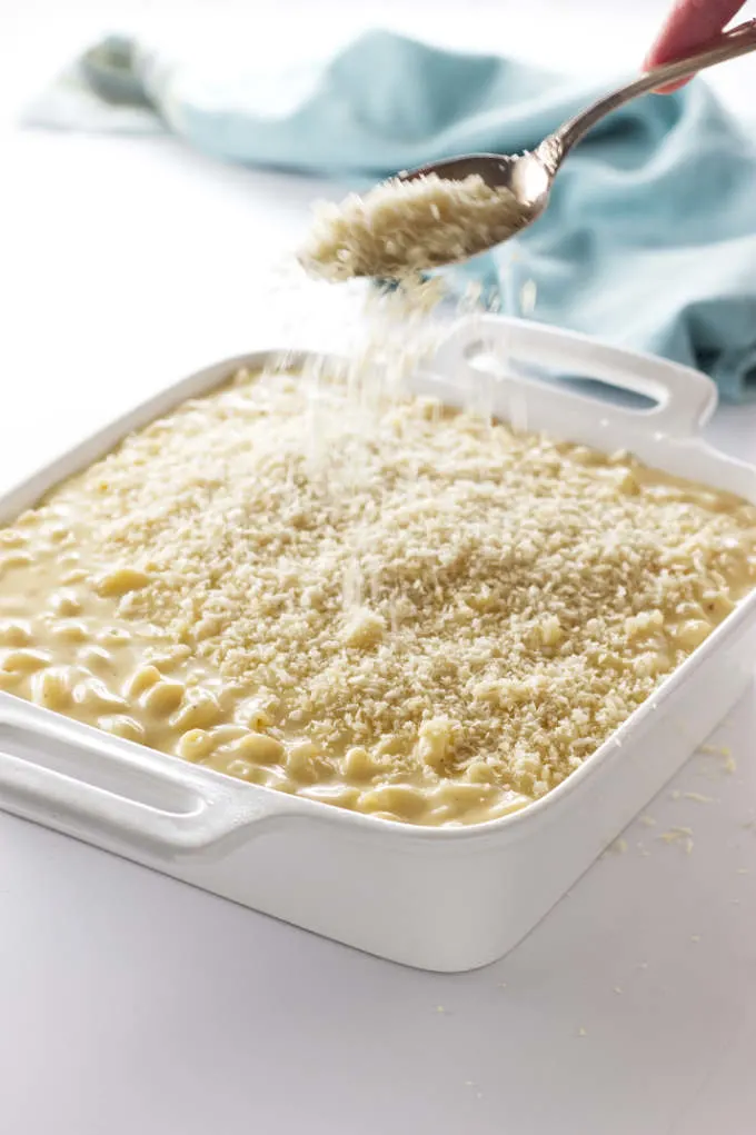 Sprinkling bread crumbs on a casserole dish of macaroni and cheese.