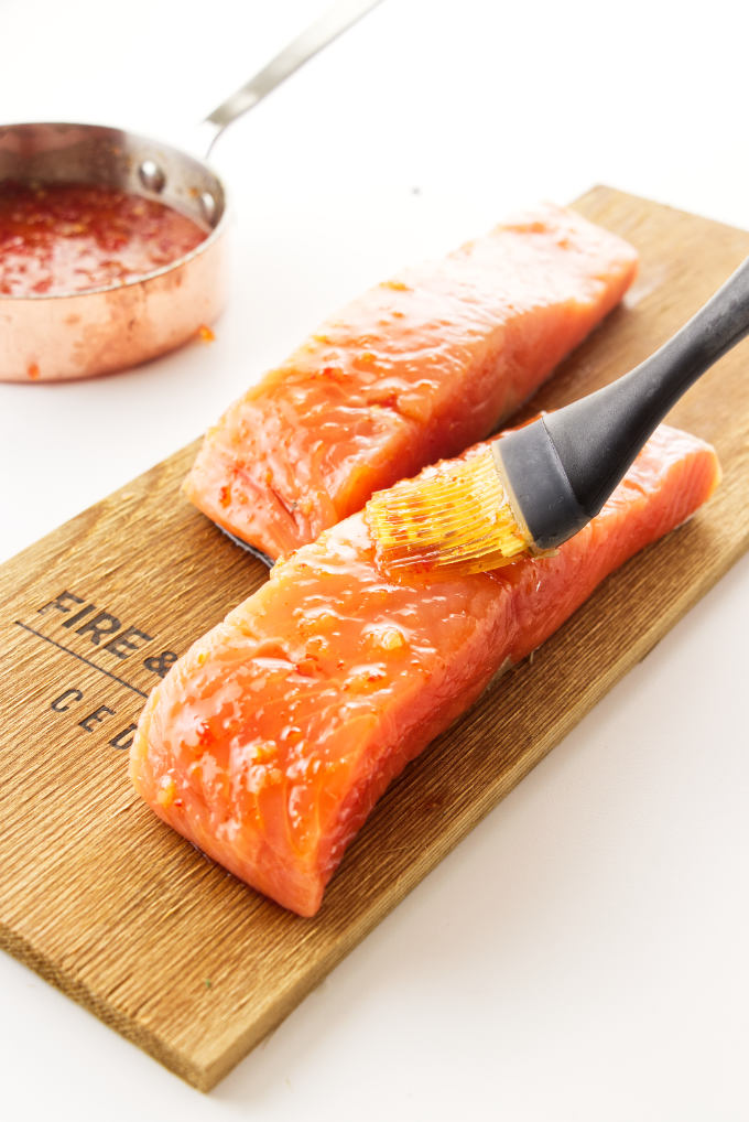 Cedar plank, two salmon fillets being brushed with Thai sweet chili sauce