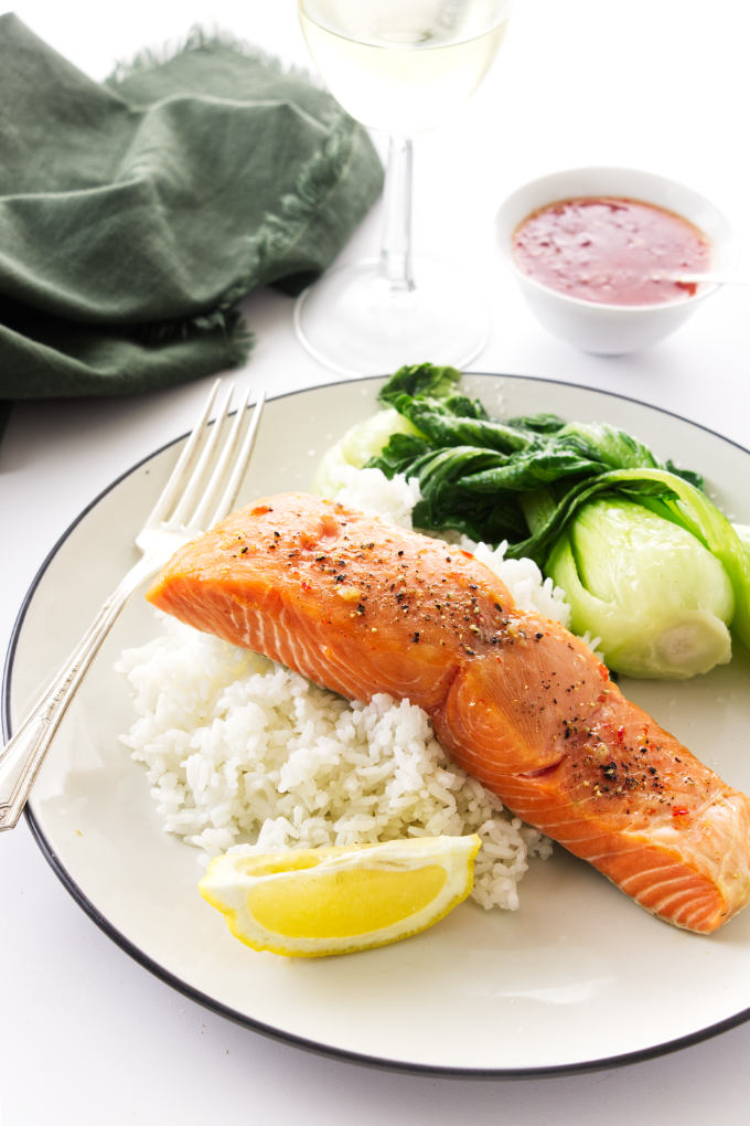 Cedar planked salmon filet on a mound of rice with bok choy a dish of warm Thai sweet chili sauce and wine in background