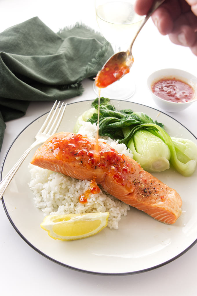 Overhead view of a serving of salmon being drizzled with Thai cilli glaze and a mound of rice