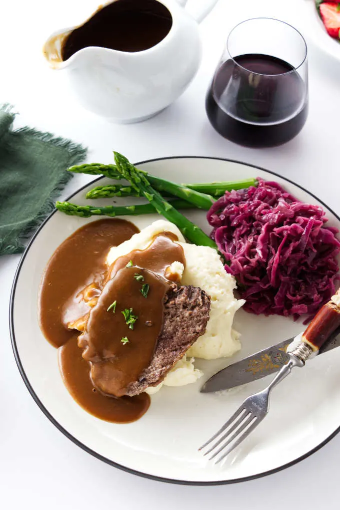 A dinner plate with a slice of roast, mashed potatoes, gravy, asparagus, and red cabbage.