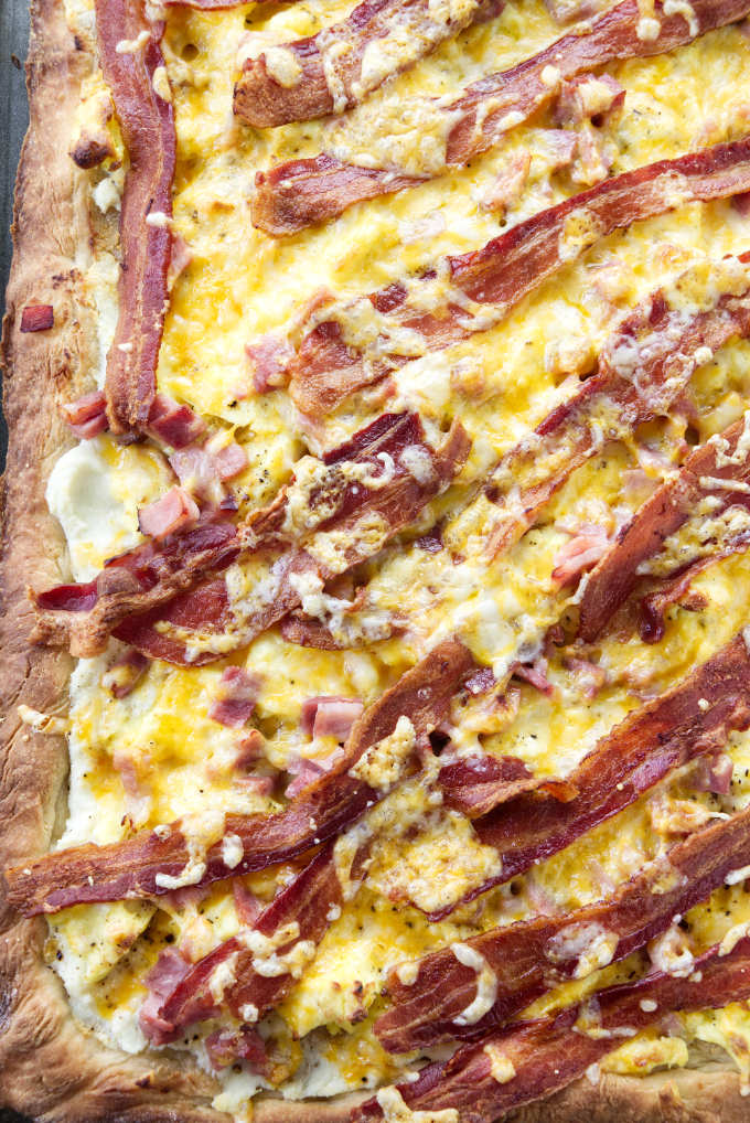 A sheet pan breakfast pizza with bacon, eggs, ham, and cheese.