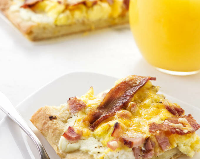 A slice of breakfast pizza next to a glass of orange juice.