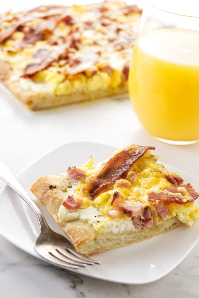 A slice of breakfast pizza next to a glass of orange juice.