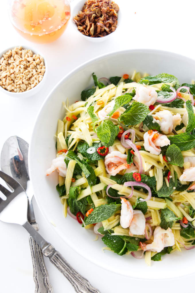 Green mango salad with shrimp in a serving bowl next to nuac mam sauce and peanuts.