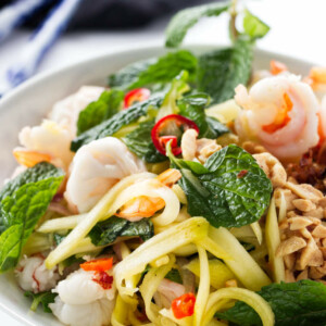 Green mango salad in a bowl with chopsticks in the background.