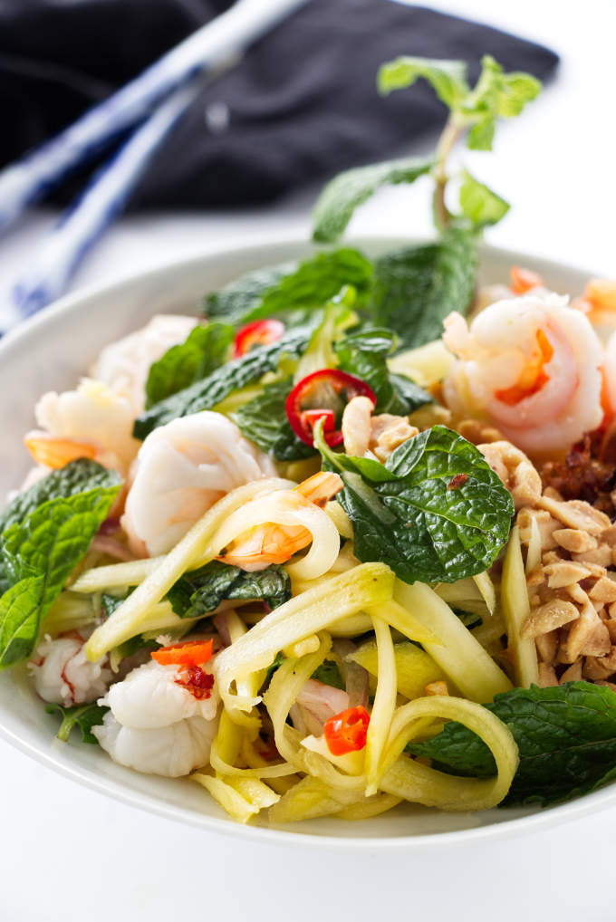 Green mango salad in a bowl with chopsticks in the background.