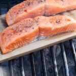 two seasoned salmon fillets being grilled on a cedar plank