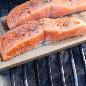 two seasoned salmon fillets being grilled on a cedar plank