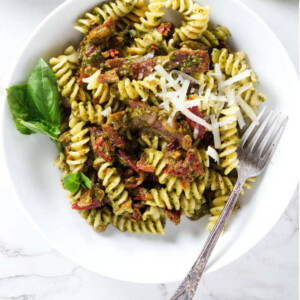 A bowl of pesto pasta with prosciutto.