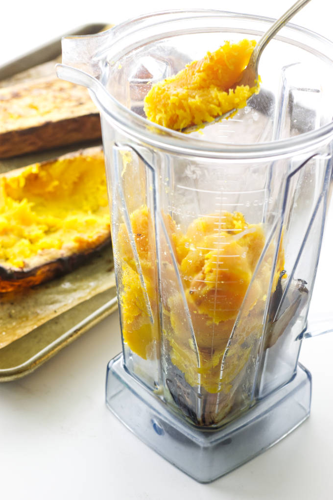 Blender with butternut squash being scooped in.