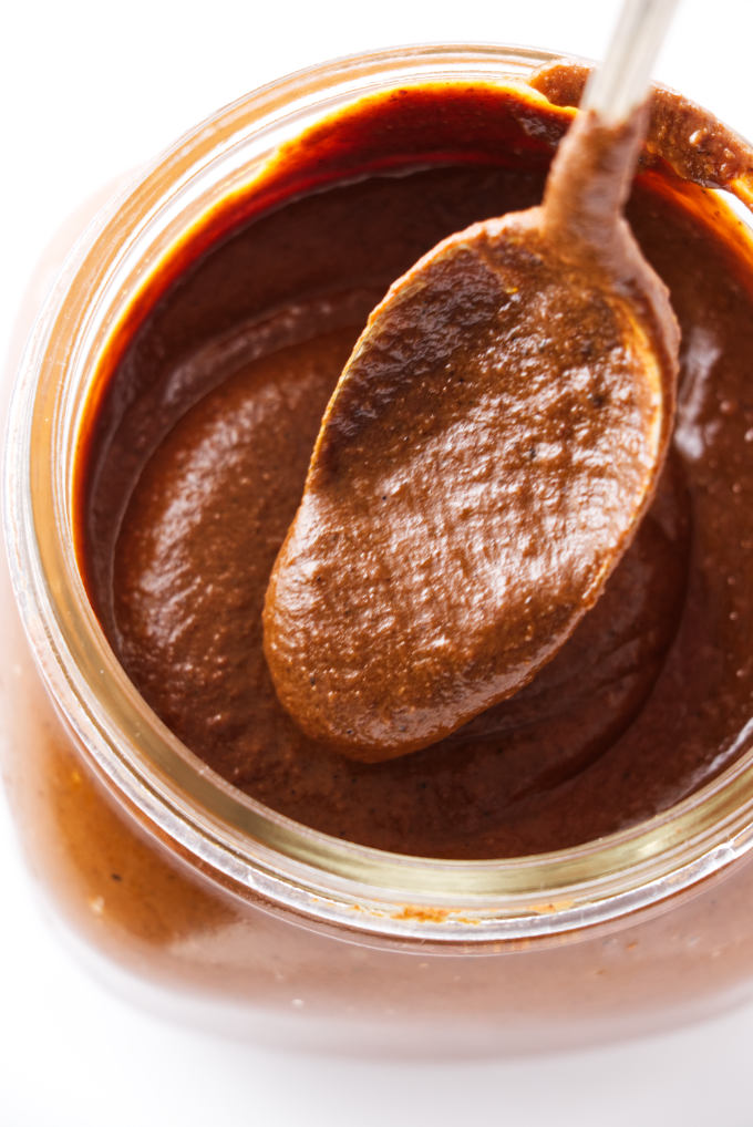 A spoon scooping mole sauce in a jar.
