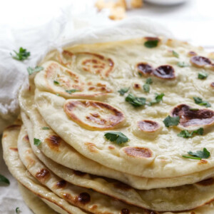 A stack of naan bread with hummus in the background.