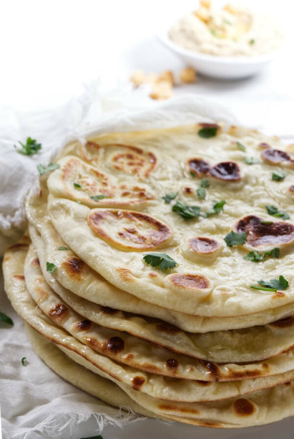 A stack of naan bread with hummus in the background.