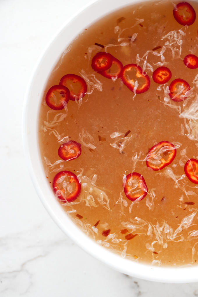 An overhead view of chili peppers and lime pulp floating on top of nuac mam sauce.