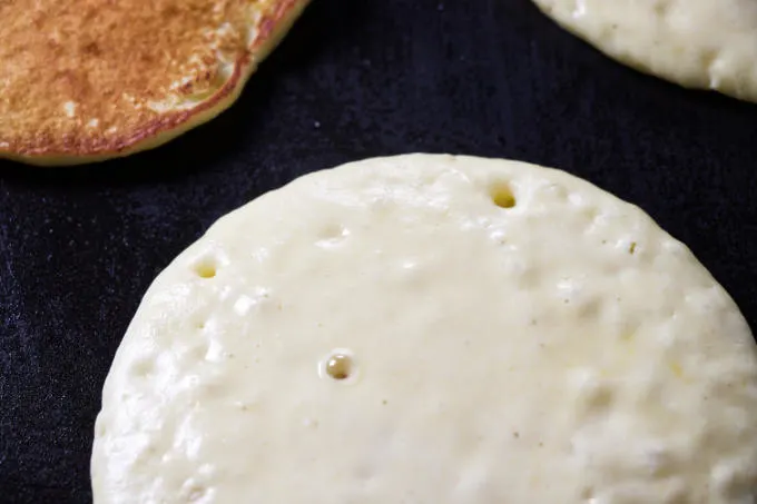 A pancake on a griddle that is ready to flip.