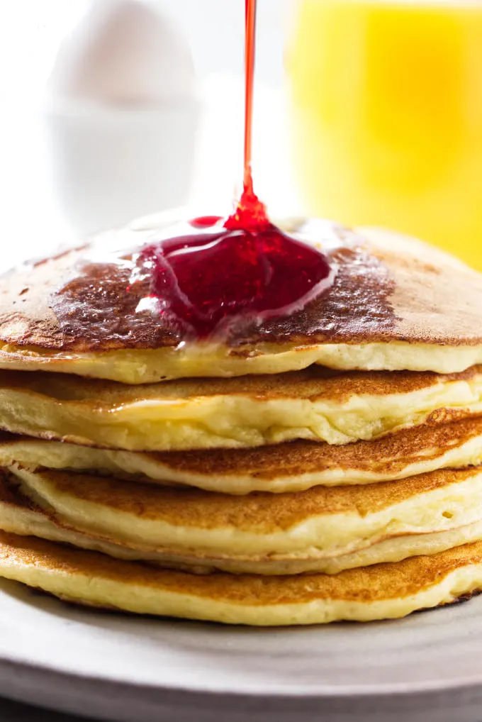 A stack of orange ricotta pancakes with a drizzle of pomegranate syrup.