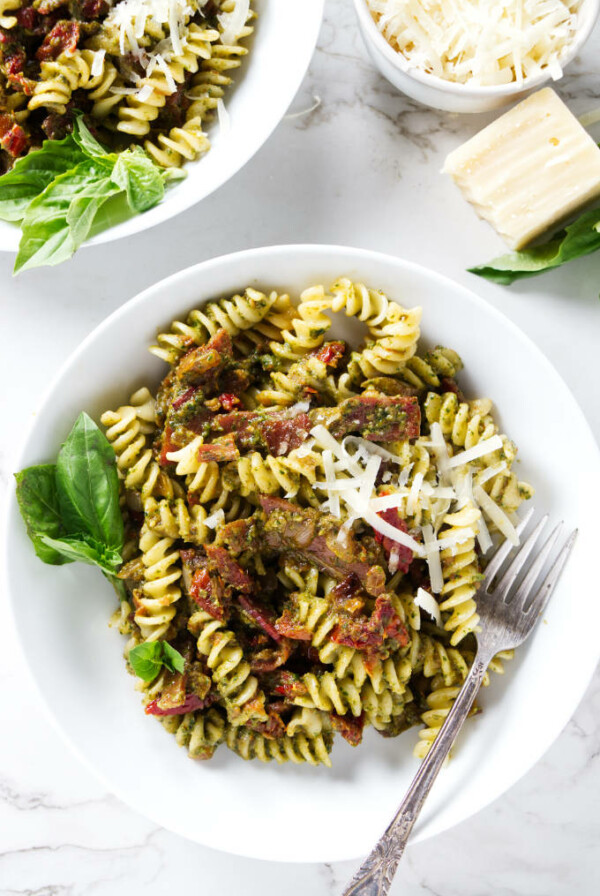 Two bowls of pesto pasta with prosciutto.