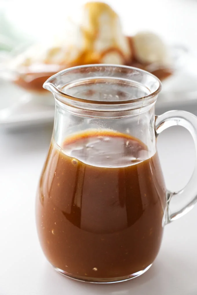 Caramel sauce in a glass pitcher with ice cream in the background.