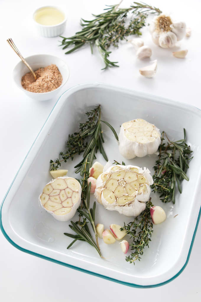 Garlic and herbs in a roasting pan, seasoning, oil, herbs and garlic in background