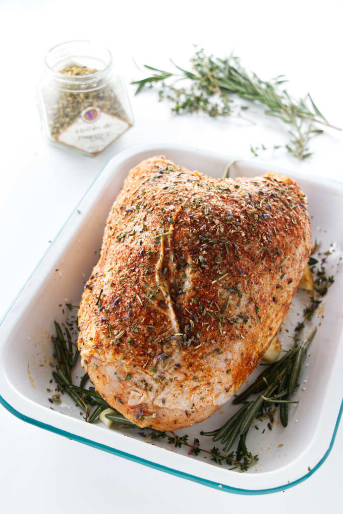 Seasoned turkey breast in roasting pan. Dried herbs and fresh herbs in background