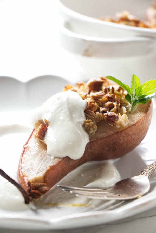 A pear half on a plate with granola and ricotta.