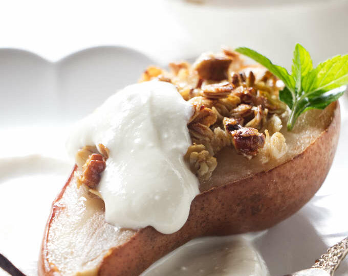 A pear half on a plate with granola and ricotta.