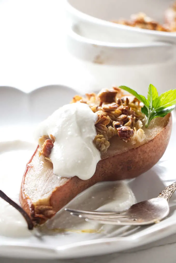 A pear half on a plate with granola and ricotta.