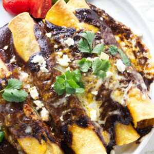 A plate with four chicken mole enchiladas and a sliced avocado.