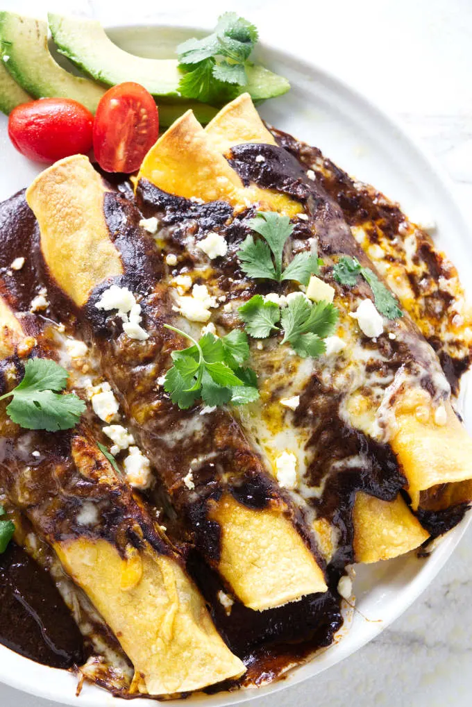 A plate with four chicken mole enchiladas and a sliced avocado.