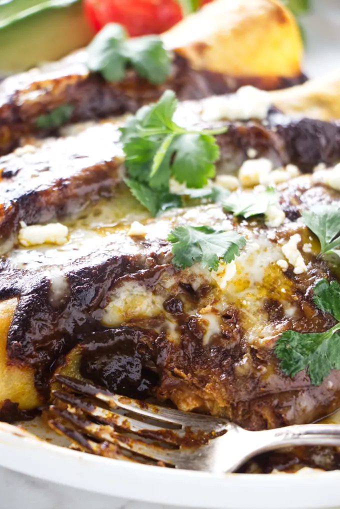 A fork on a plate with chicken mole enchiladas.