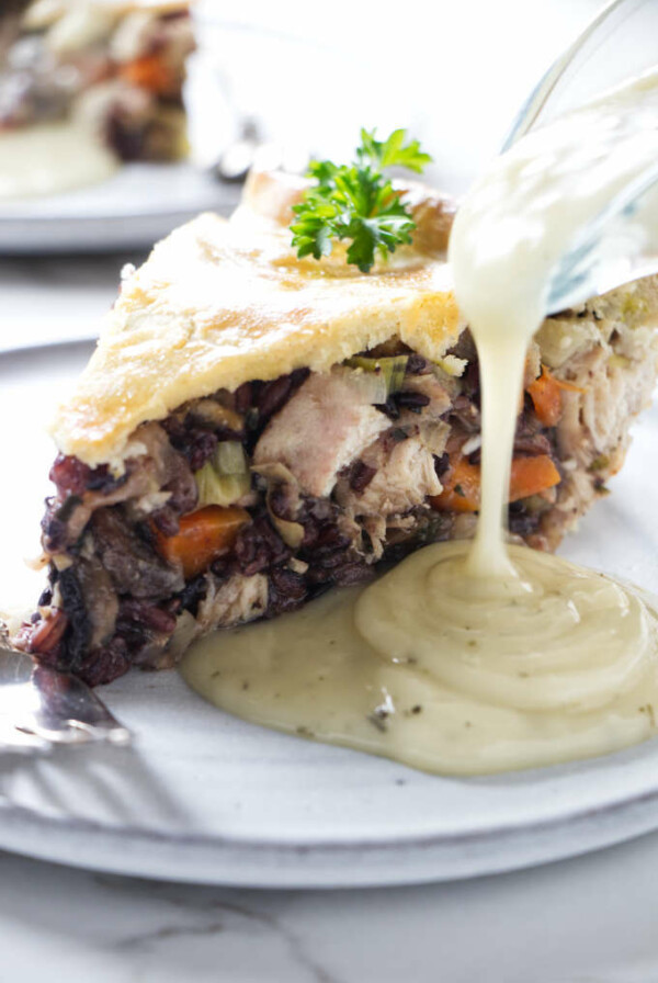 White wine sauce being poured next to a slice of chicken pot pie.