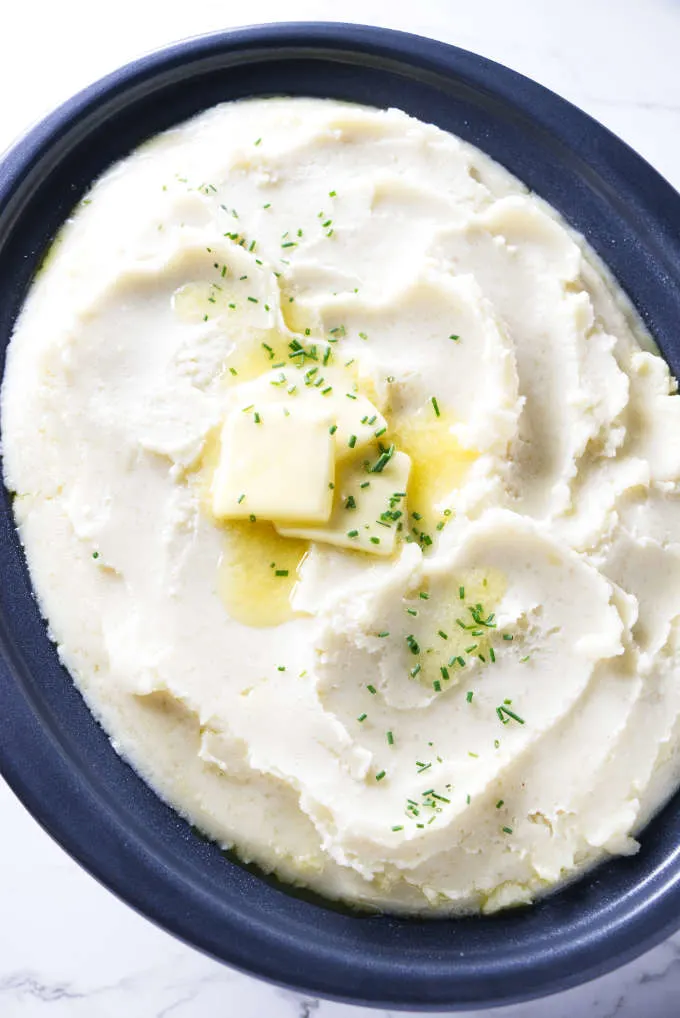 Butter and chives on mashed potatoes in a crockpot.
