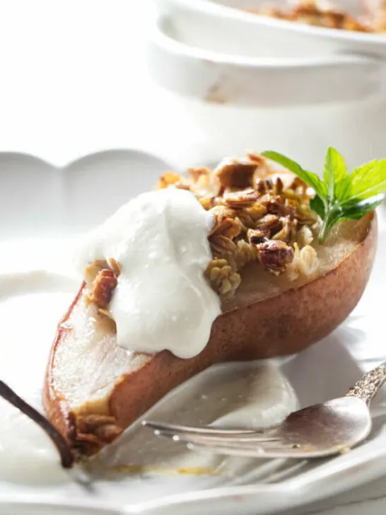 A pear half on a plate with granola and ricotta.