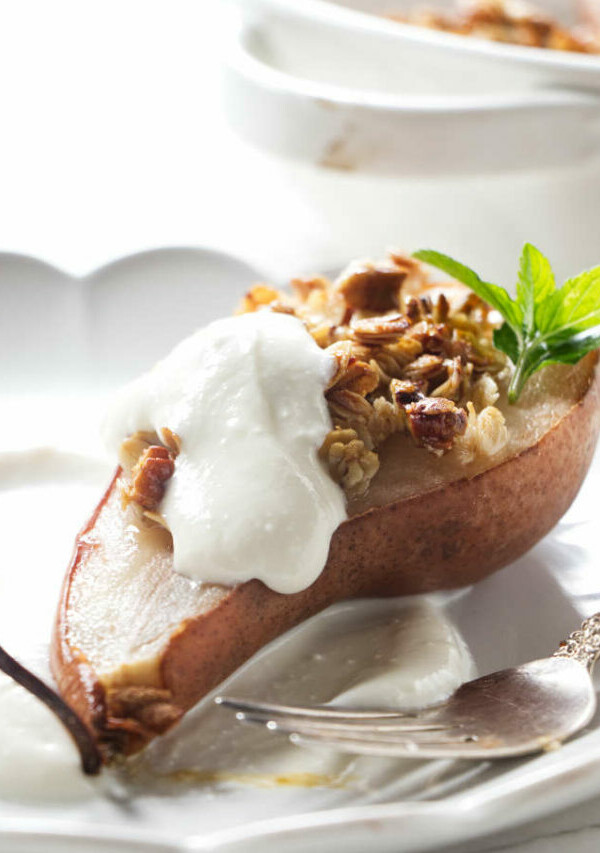 A pear half on a plate with granola and ricotta.