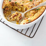 A spoon in a casserole dish with corn pudding.