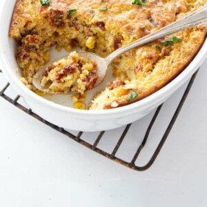 A spoon in a casserole dish with corn pudding.