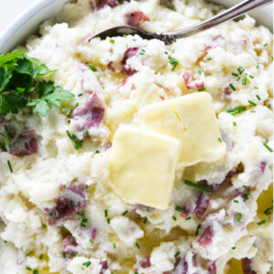 Chives and butter on top of a bowl of mashed red potatoes.