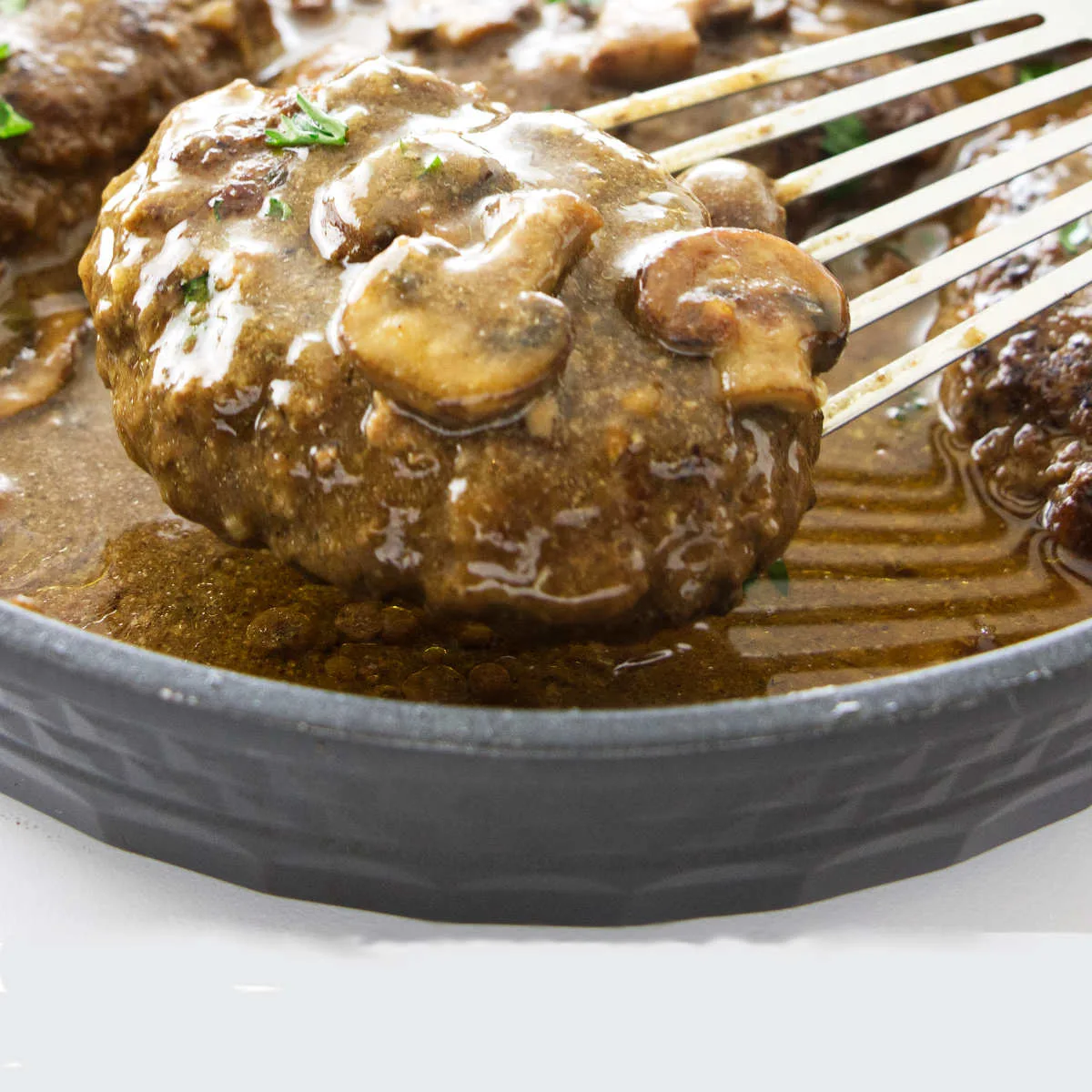 A spatula removing a Salisbury steak from a skillet.