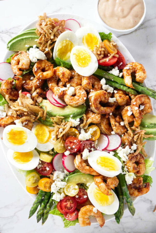 A large shrimp Louie salad next to Louie salad dressing.