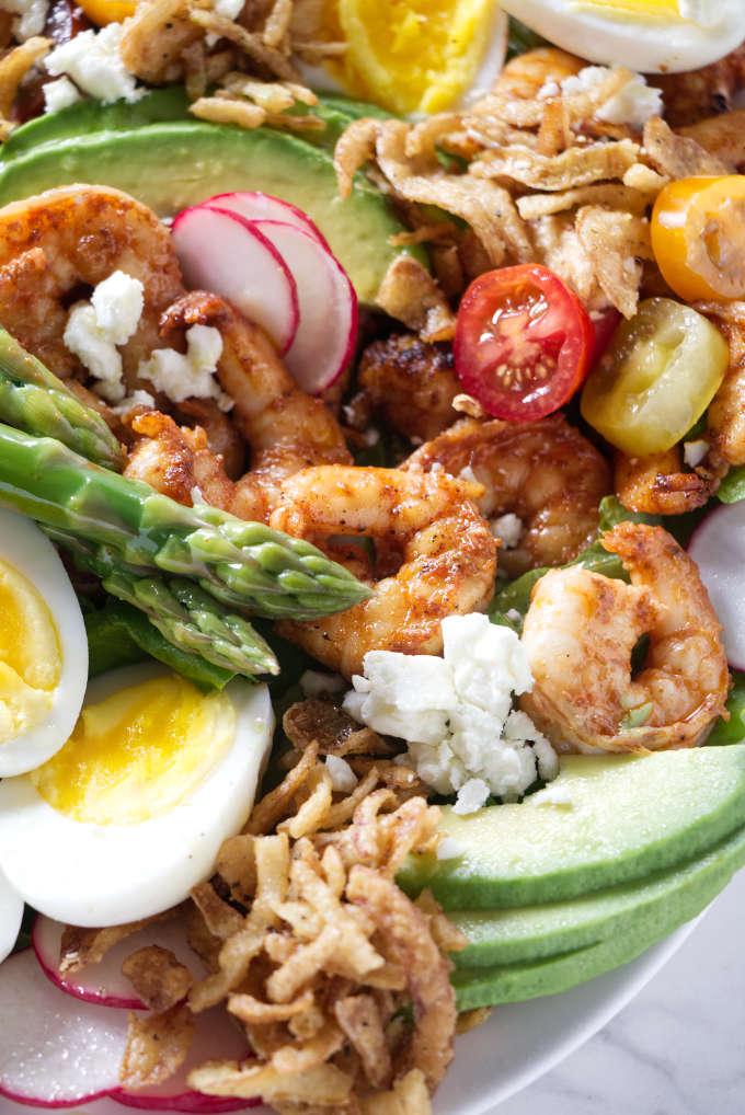 Seasoned shrimp, vegetables, cheese, eggs, and crispy fried onions on a salad.