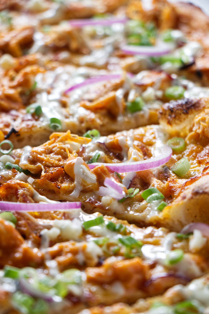 Several slices of buffalo chicken pizza with green onions sprinkled on top.