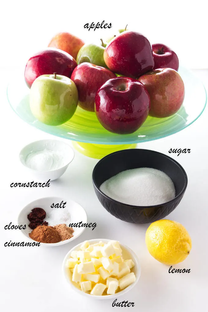 a variety of red and green apples with baking ingredients on a white work surface.