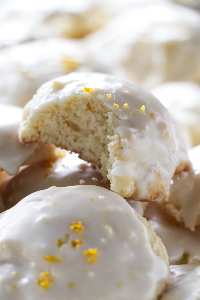 A partially eaten lemon ricotta cookie on a stack of cookies.