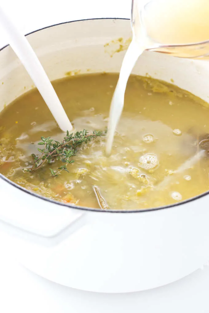 Chicken broth being poured into a soup pot of pea soup