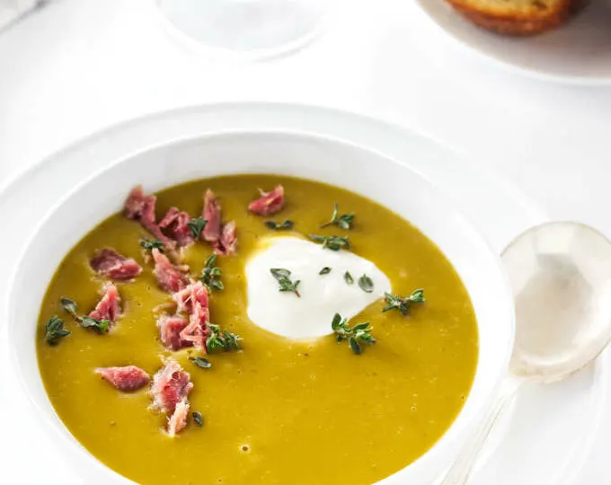 Overhead view of smoky split pea soup, glass of wine , napkin and bread in background