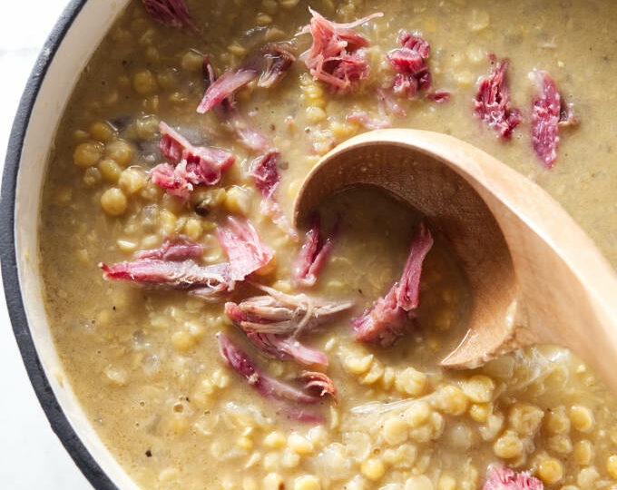 A pot of Swedish pea soup with yellow peas and shreds of ham hock meat on top.