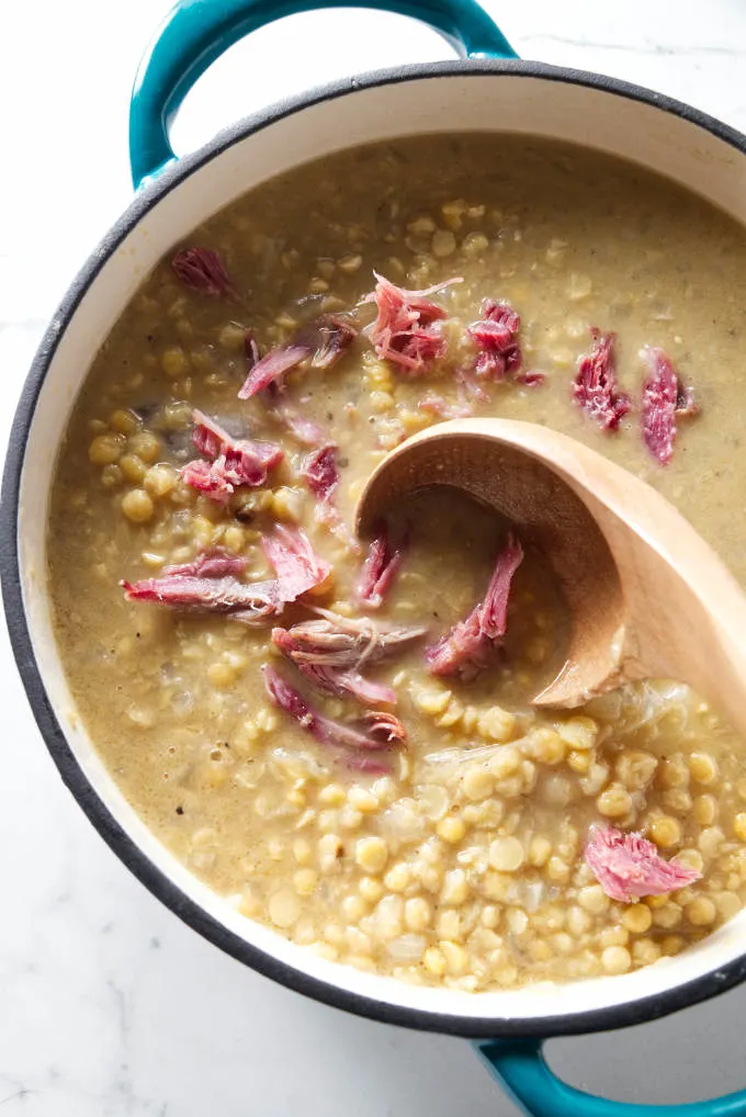 A pot of Swedish pea soup with yellow peas and shreds of ham hock meat on top.