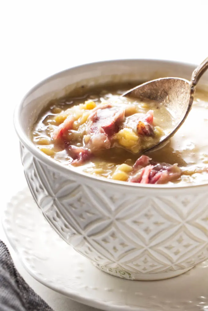 A spoon scooping pea and ham soup from a bowl.