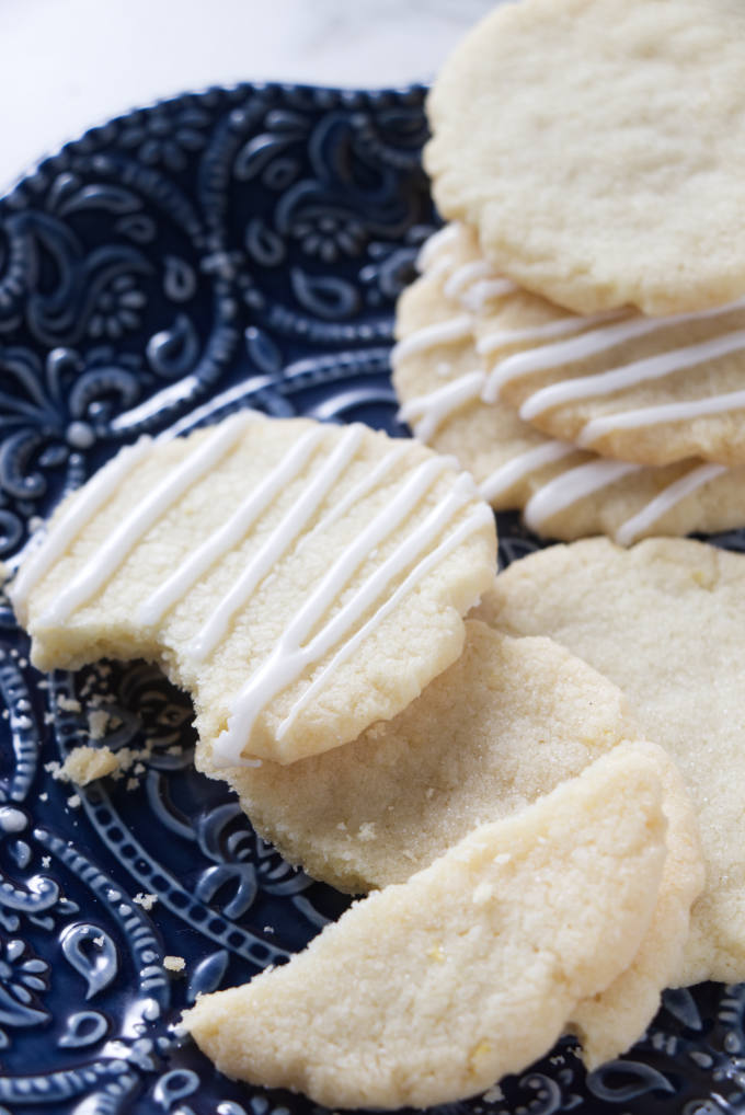 A few lemon cookies on a plate showing how crisp they get when broken in half.